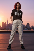 GRIT Women's Heavyweight Boxy Tee Black – RESILIENT RISE graphic streetwear, model wearing boxy fit tee with wide-leg trousers and black boots, rooftop city skyline golden hour editorial